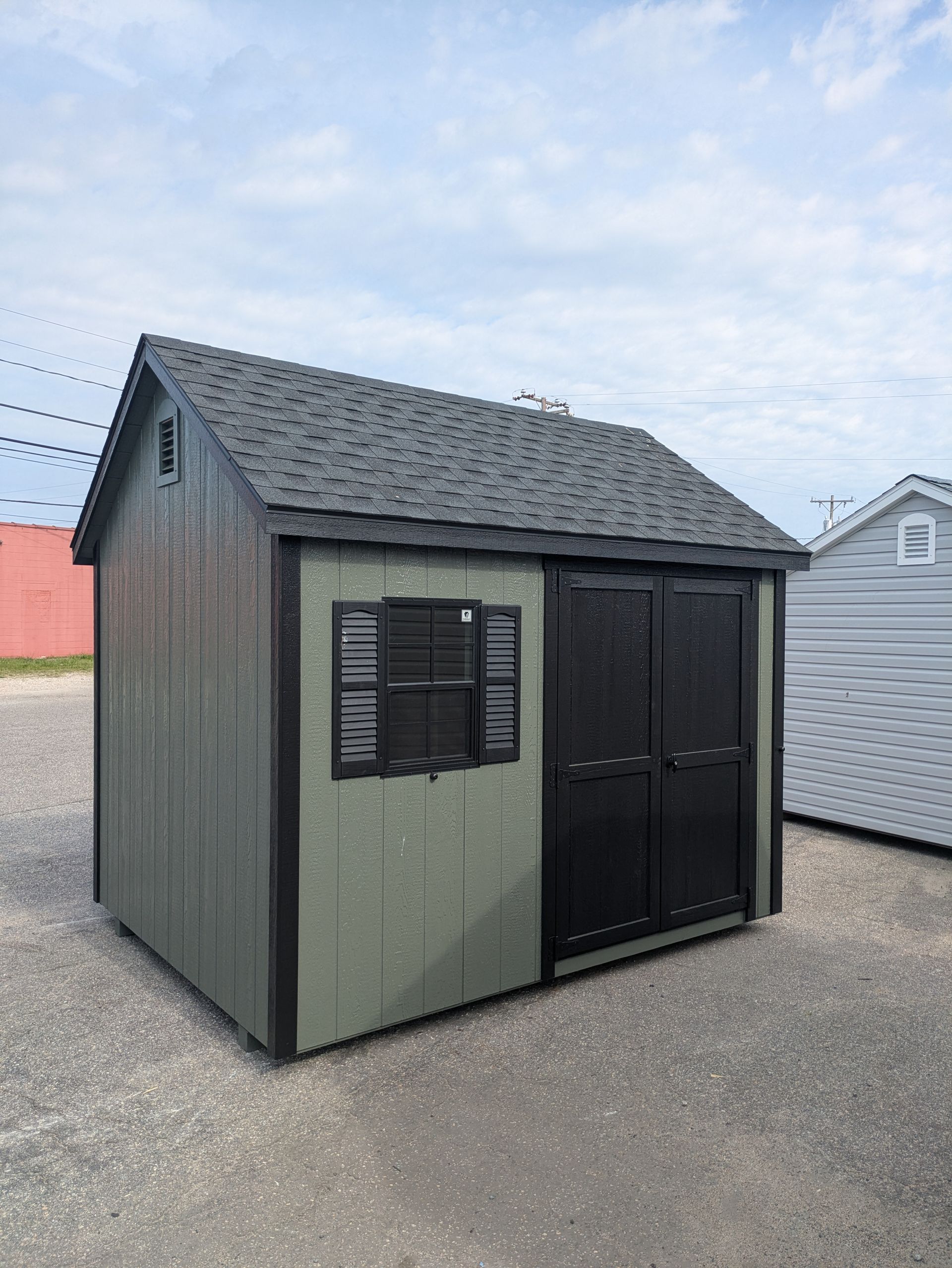 A small green shed with a black door and window is sitting in a parking lot.