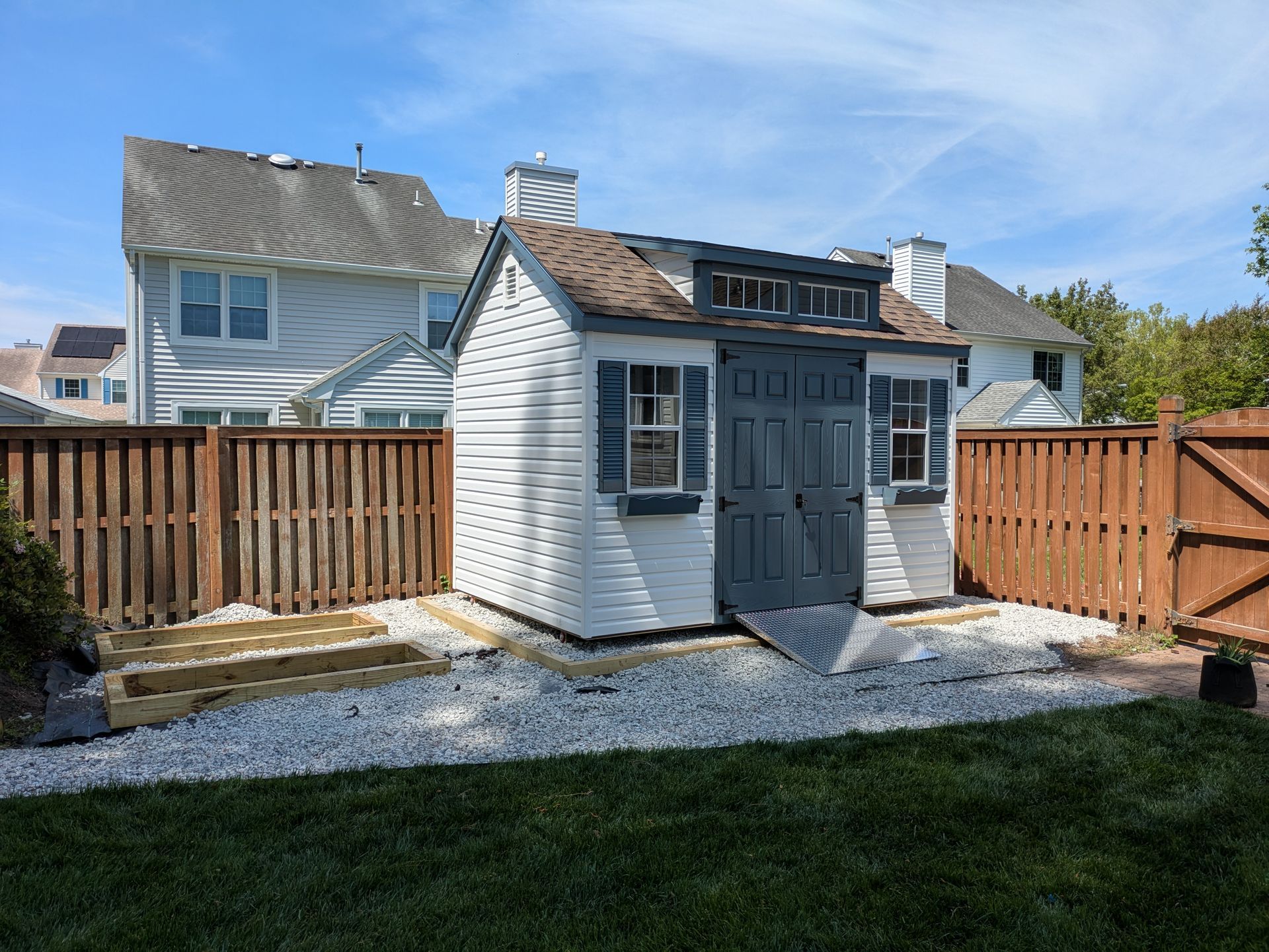A white shed with a wooden fence in front of a house.