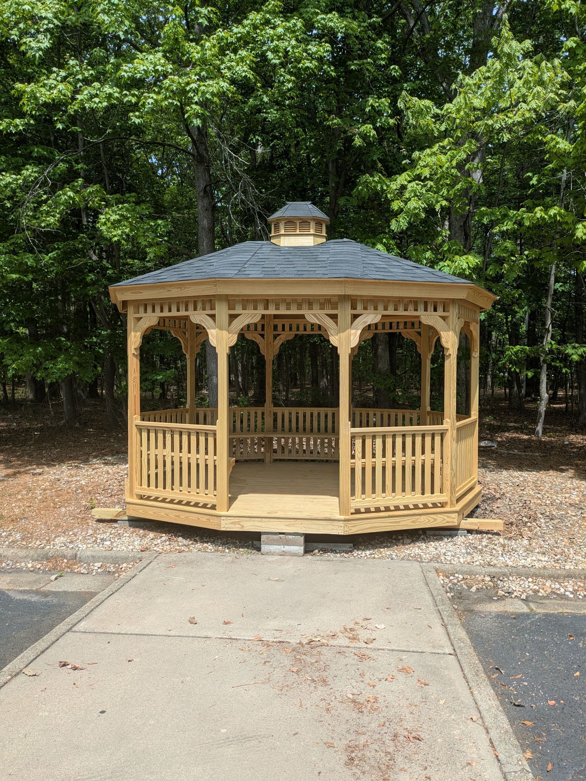 A wooden gazebo is sitting on the side of a road in the middle of a forest.