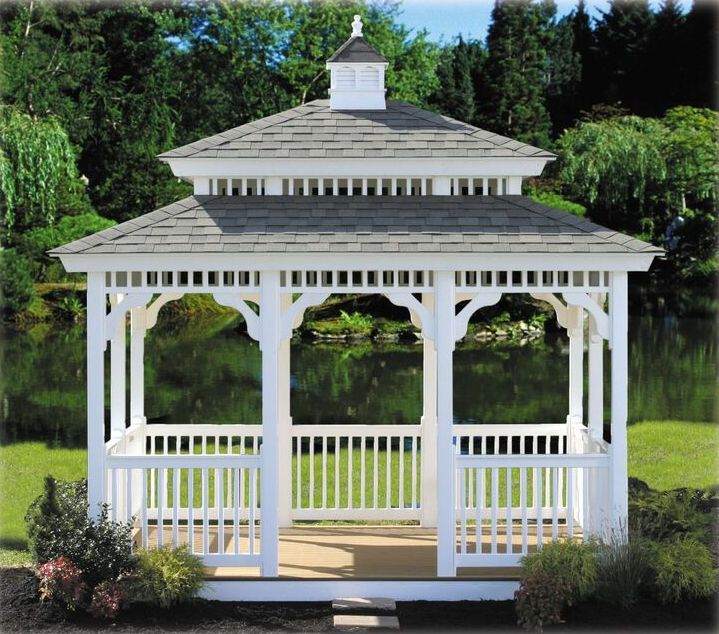 A white gazebo with a gray roof sits in the middle of a lush green field