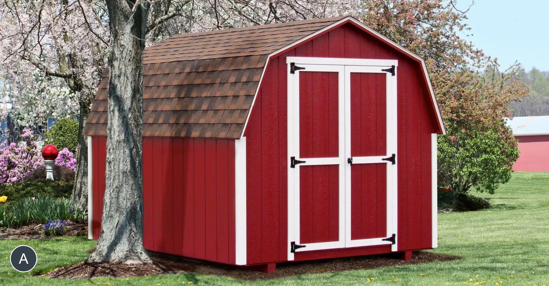 Red barn-style shed with white trim and brown roof in a grassy yard with a tree.