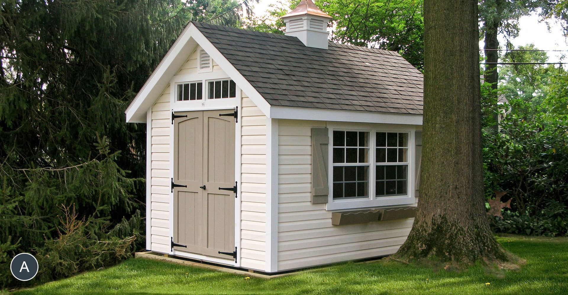 White garden shed with brown doors, window, and a copper chimney. Green grass and trees surround it.