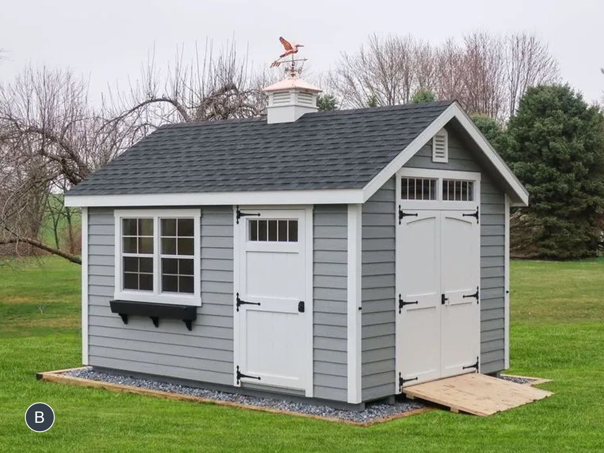A gray and white shed with a black roof is sitting on top of a lush green field.