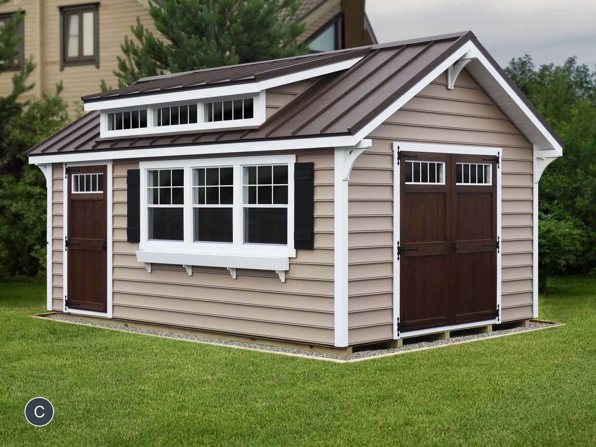 Tan shed with brown trim, doors, and metal roof, set on grass. Features include white-framed windows and a dormer.