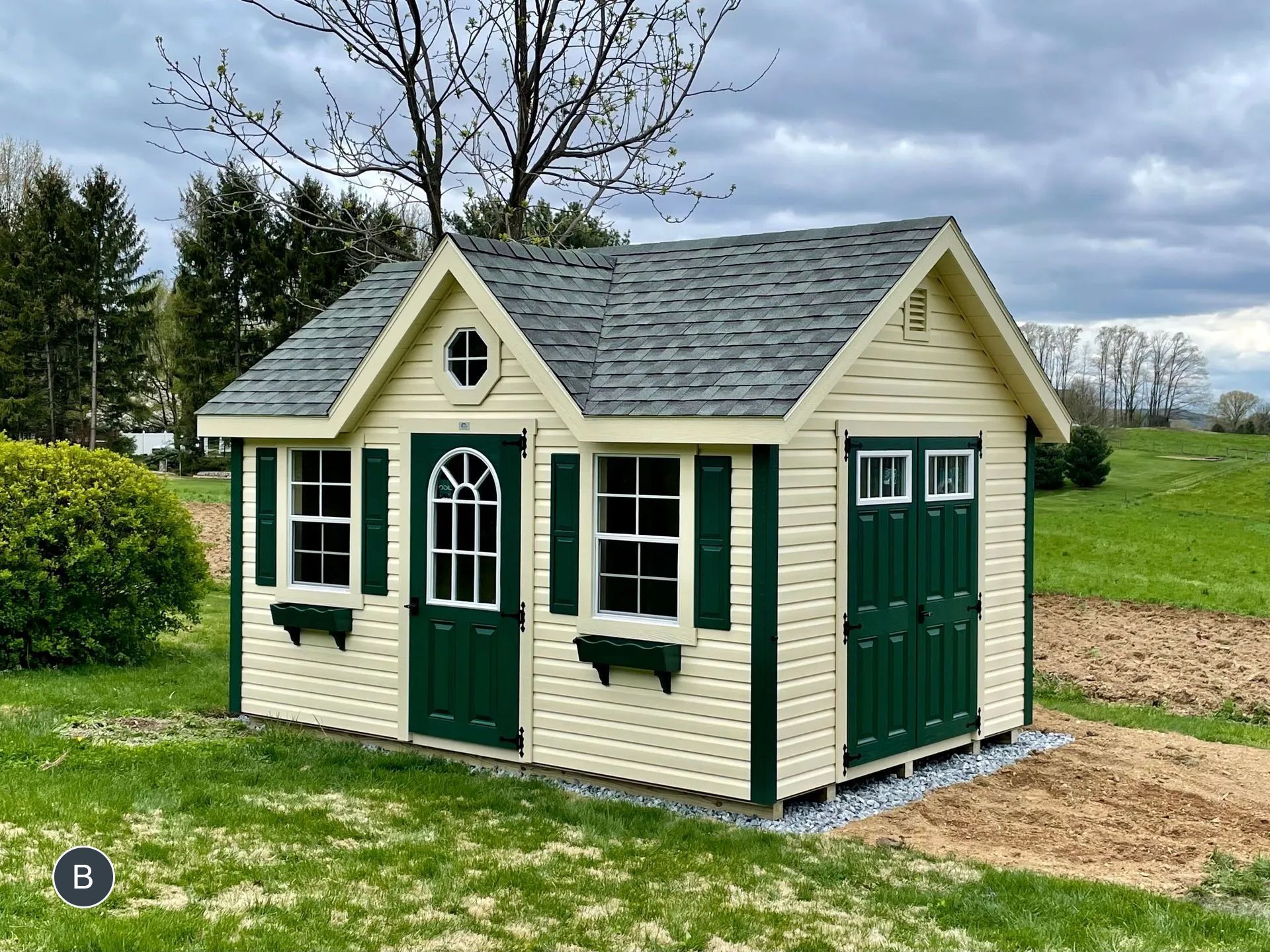A white and green shed is sitting in the middle of a grassy field.