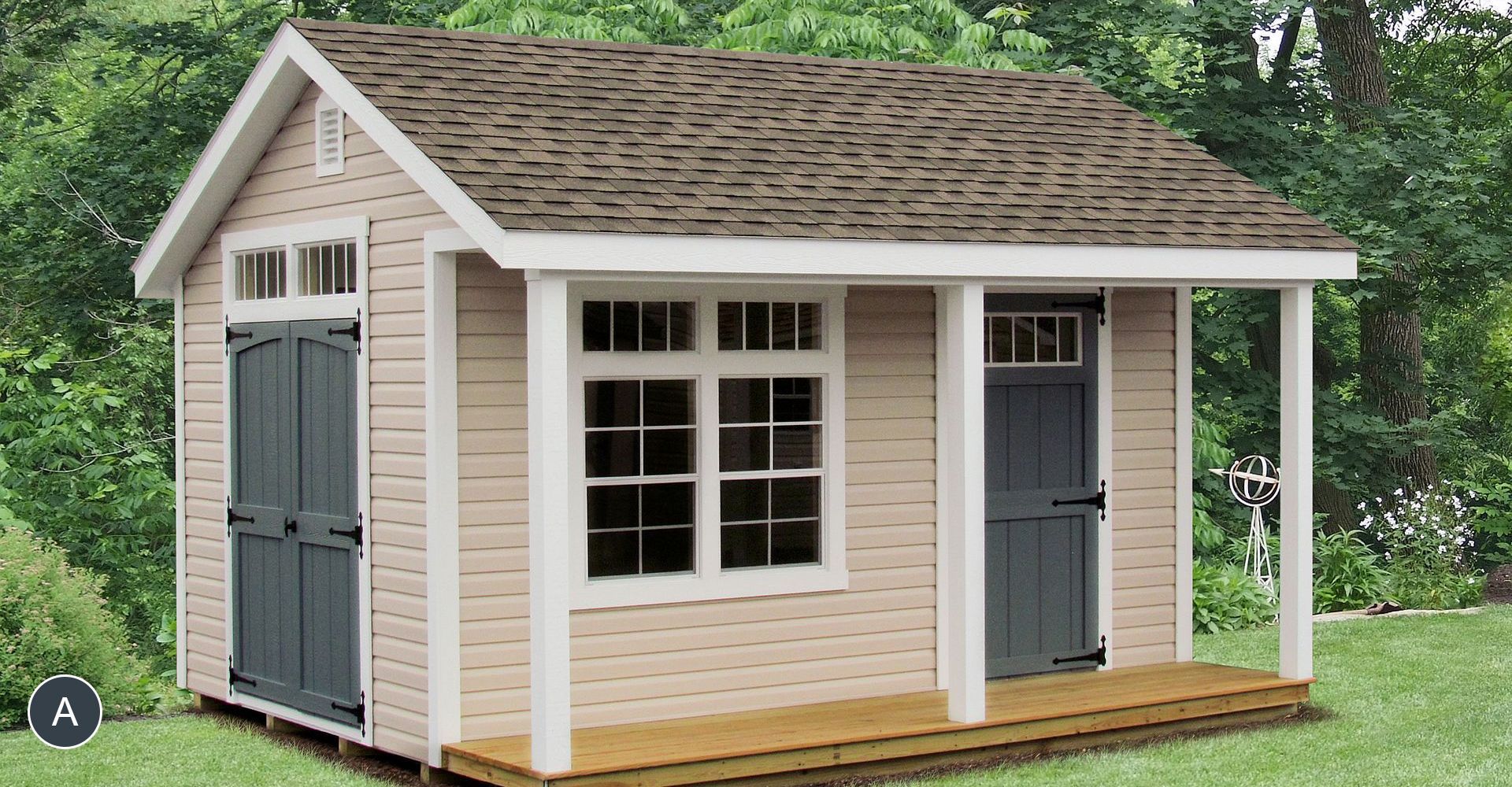 Tan shed with a porch, two green doors, and a window. The roof is brown, and the setting is a grassy yard.