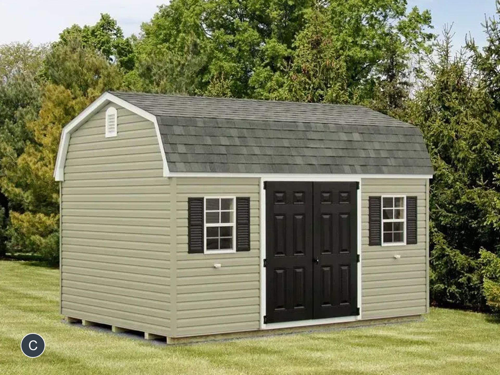 A barn with black doors and windows is sitting in the middle of a lush green field