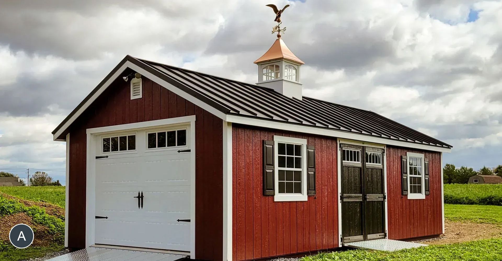 Red storage shed with a white garage door, black shutters, and a copper weathervane on the roof. The shed is in a field.