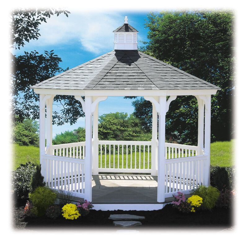 A white gazebo with a gray roof sits in the middle of a lush green field
