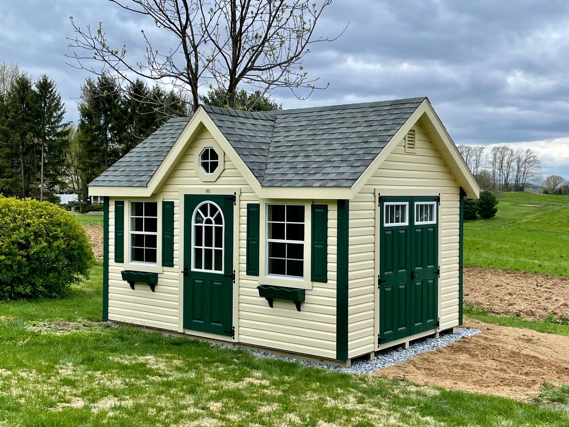 A white and green shed is sitting in the middle of a grassy field.