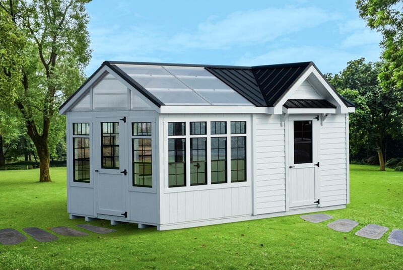 A white shed with a black roof is sitting on top of a lush green field.