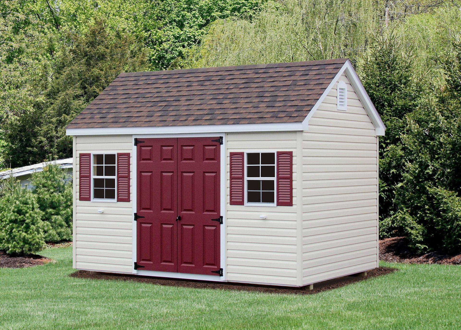 A white shed with red doors and shutters is sitting in the grass.