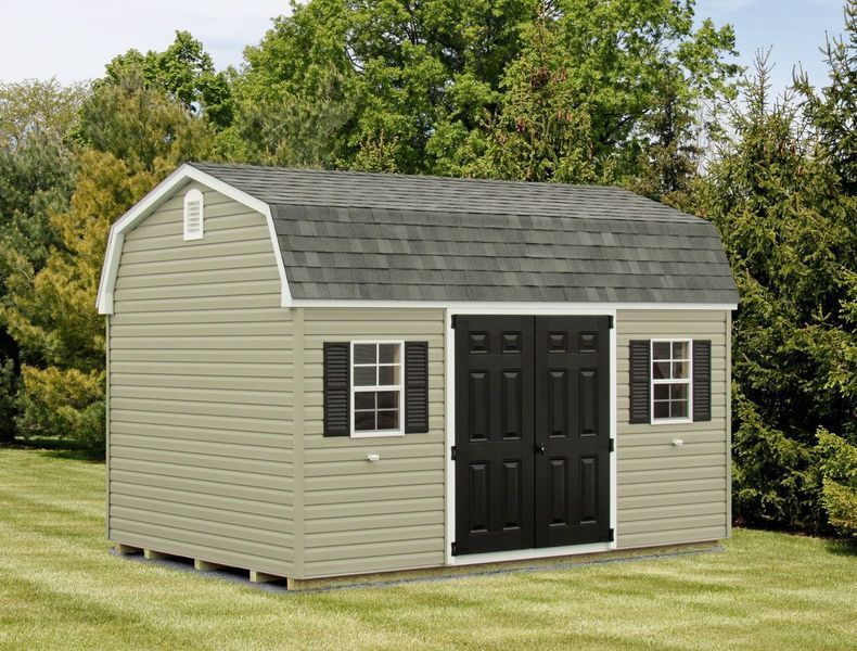 A white barn with black doors and shutters is sitting on top of a lush green field.