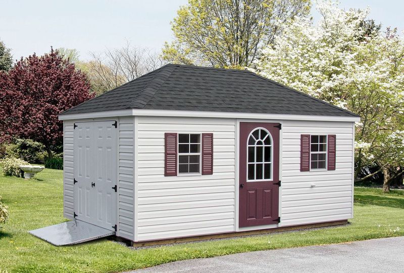 A white shed with a red door and shutters is sitting on top of a lush green field.