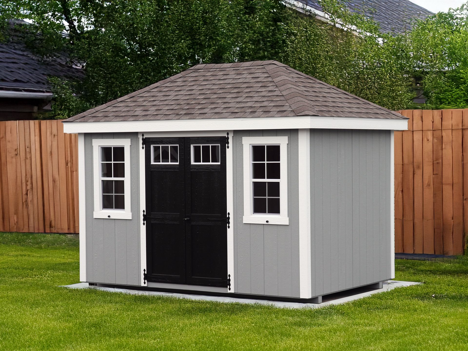 A gray shed with a black door and windows is sitting on top of a lush green lawn.