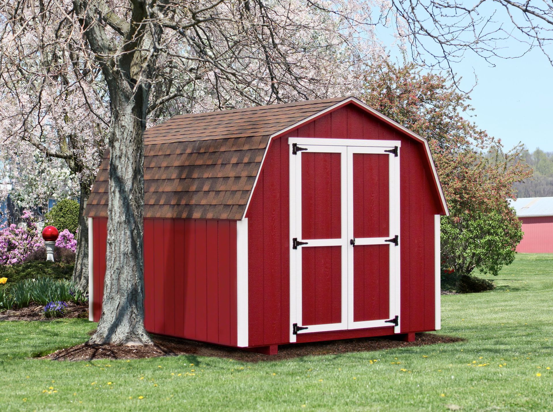 A red barn is sitting in the middle of a grassy field next to a tree.
