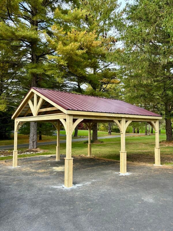 A wooden gazebo with a red roof is sitting in the middle of a parking lot.