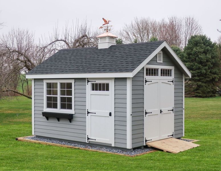 A gray and white shed with a black roof is sitting on top of a lush green field.