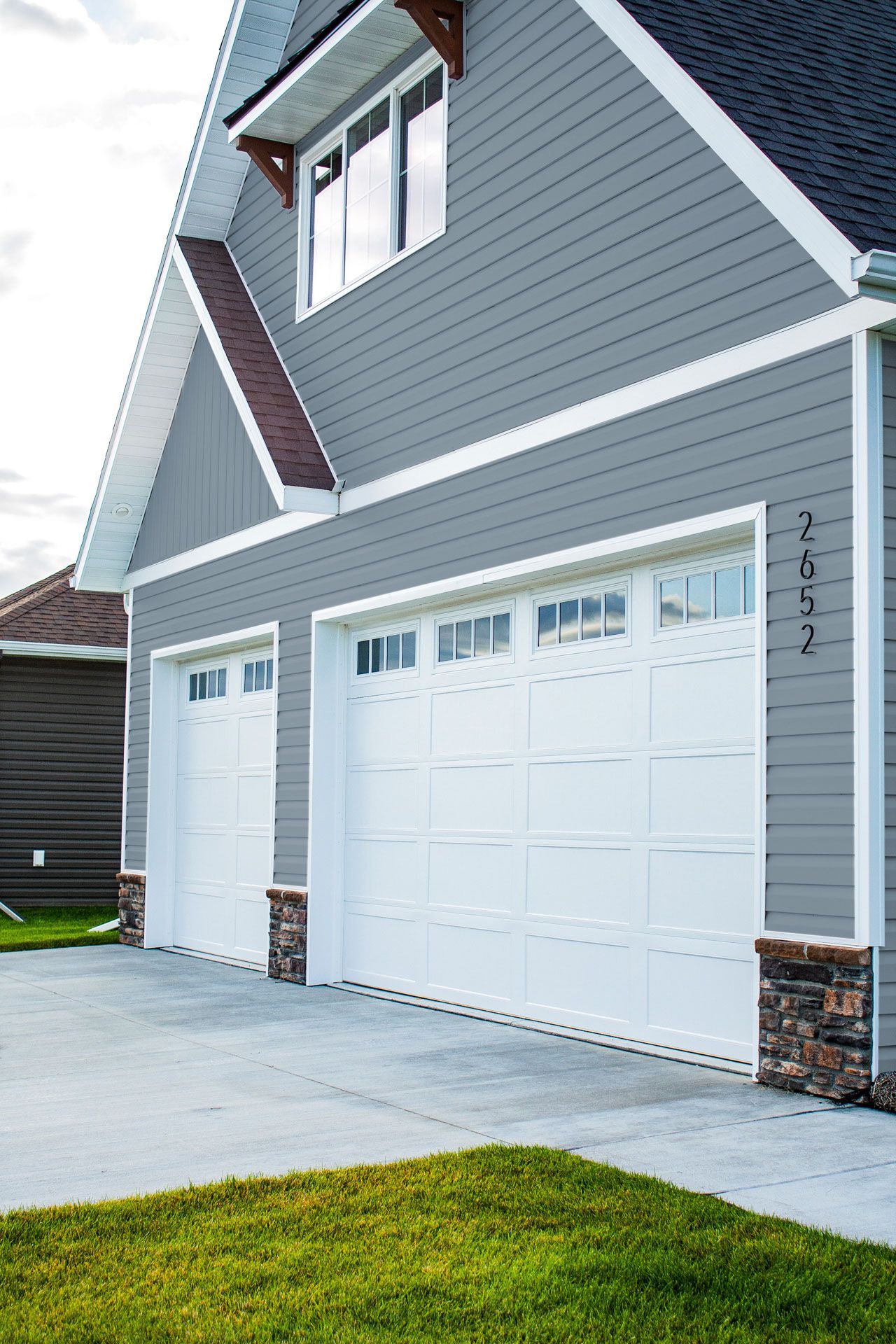 A house with three white garage doors and a gray siding.