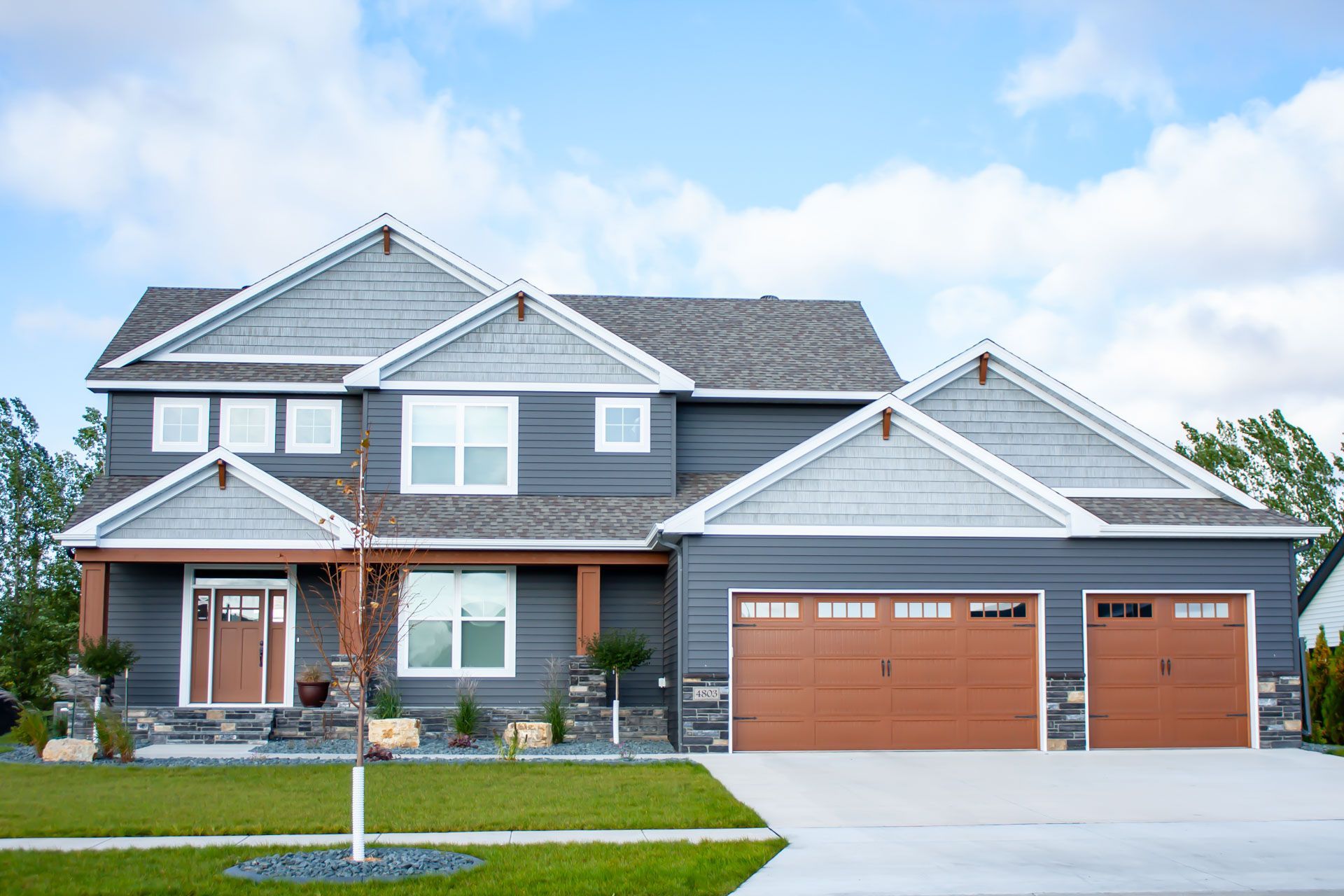 A large house with three garage doors is sitting on top of a lush green lawn.
