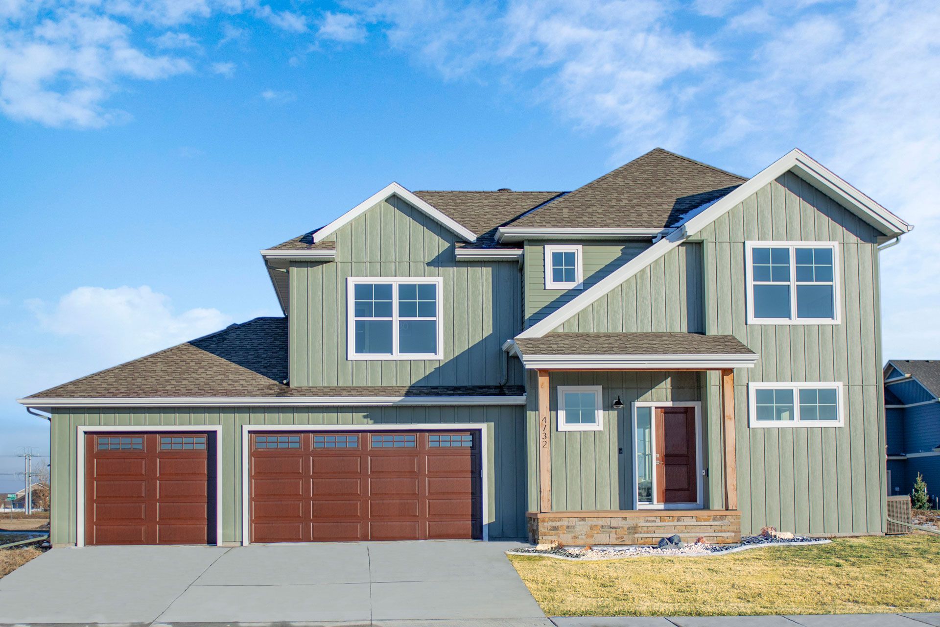 A large green house with brown garage doors and a blue sky in the background.