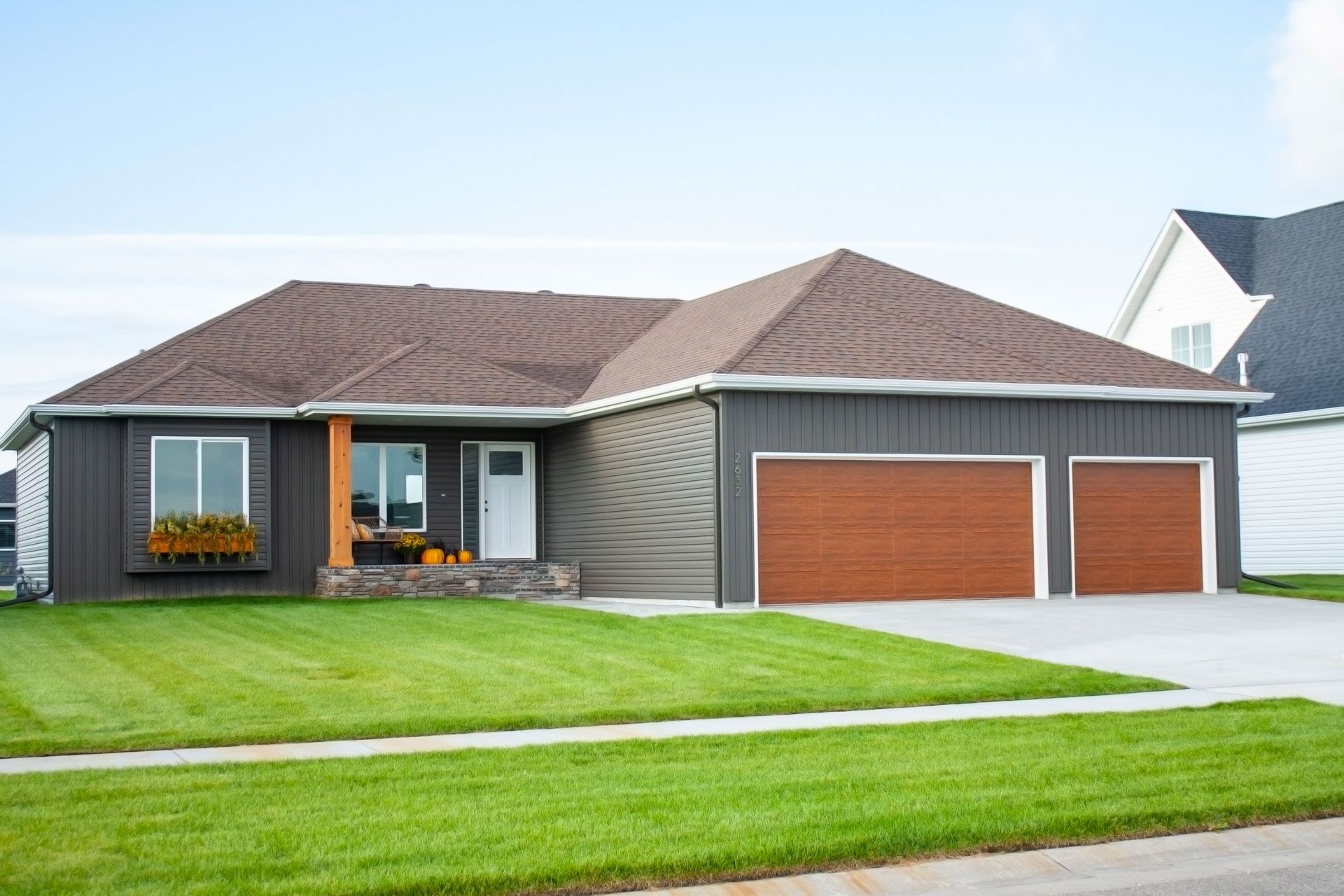 A large house with two garage doors is sitting on a lush green lawn.