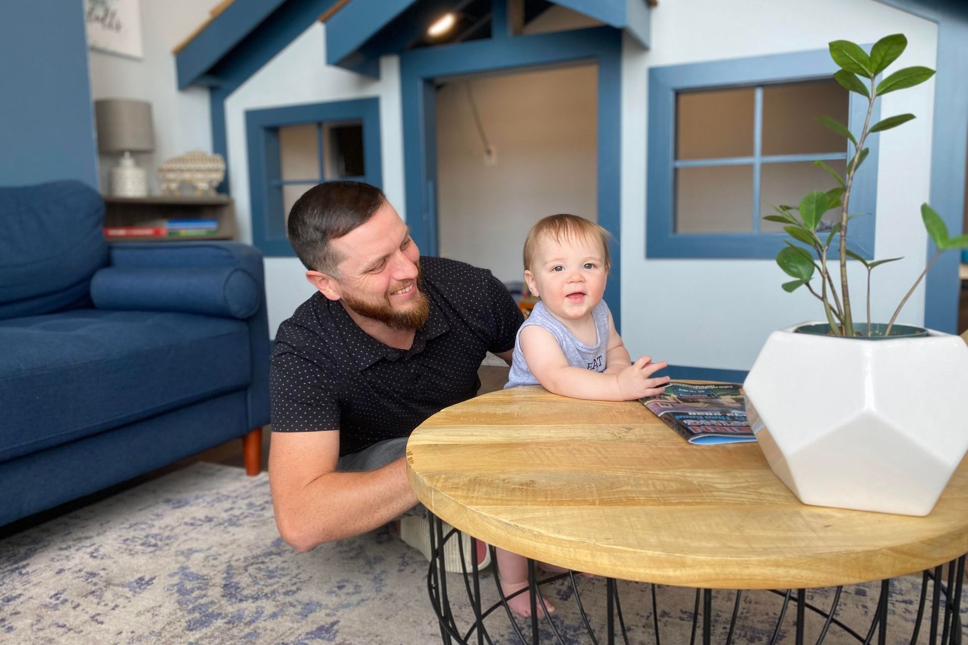 A man and a baby are sitting in front of a playhouse.