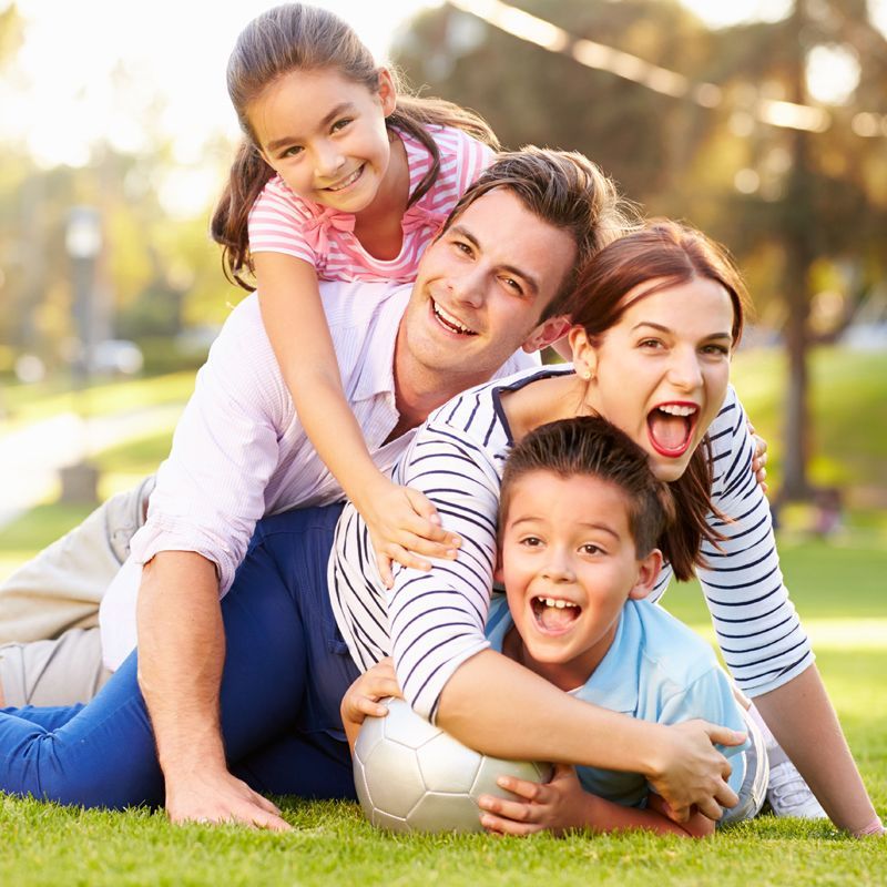 A family is playing with a soccer ball in the grass.