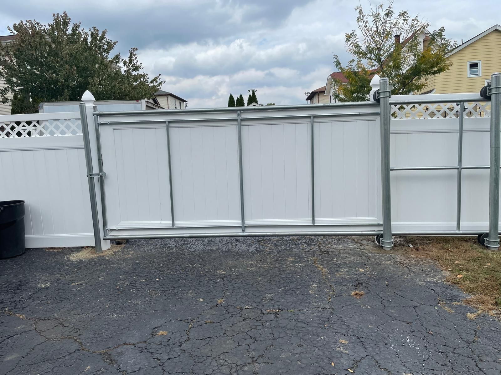 A white fence with a black trash can in front of it