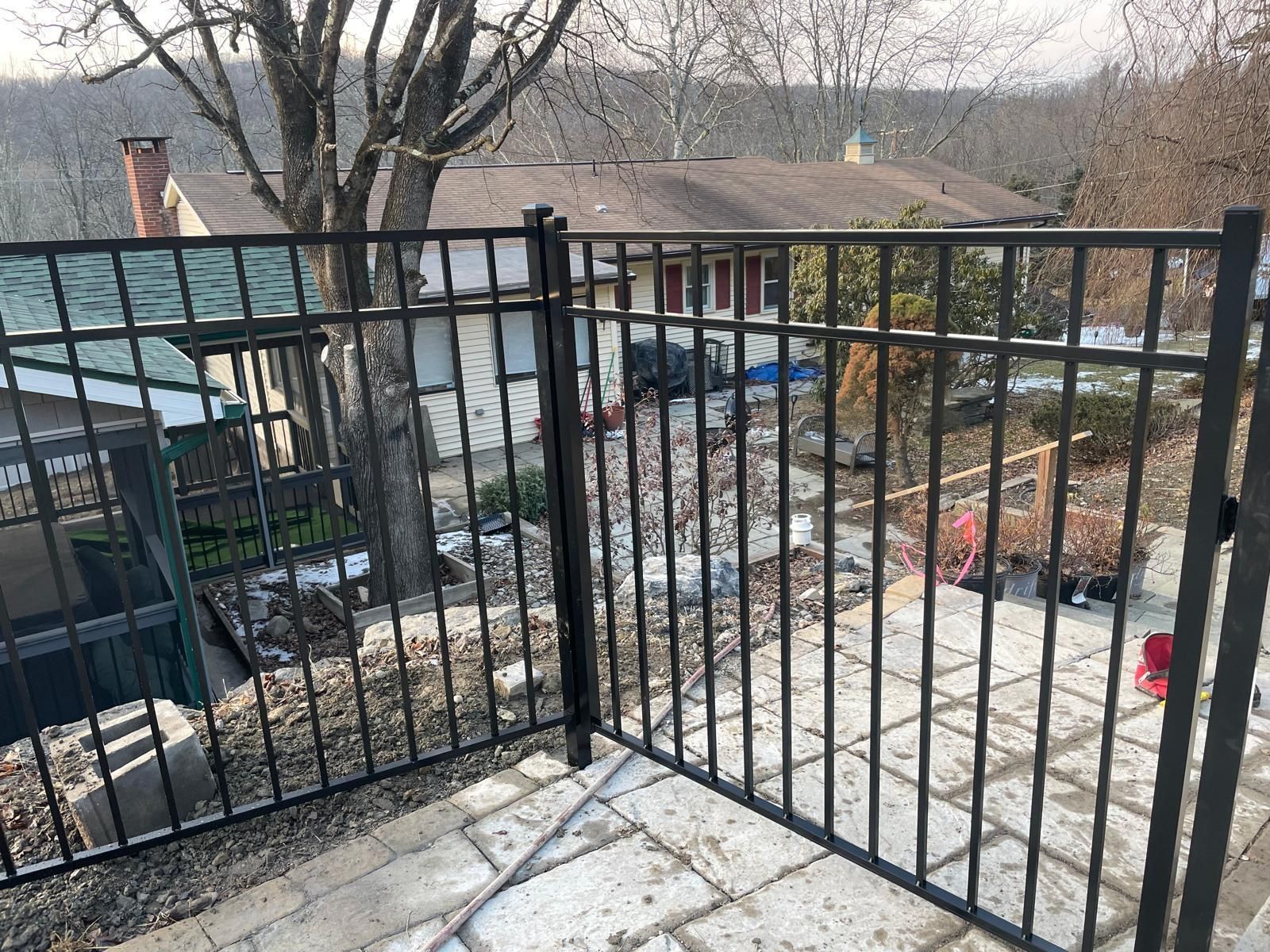 A black metal fence is sitting on top of a patio next to a house.