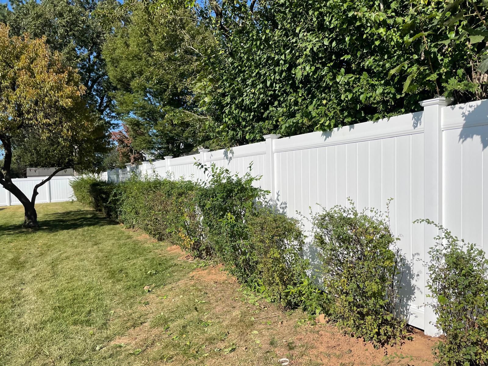 A white fence surrounds a lush green yard with trees and bushes.