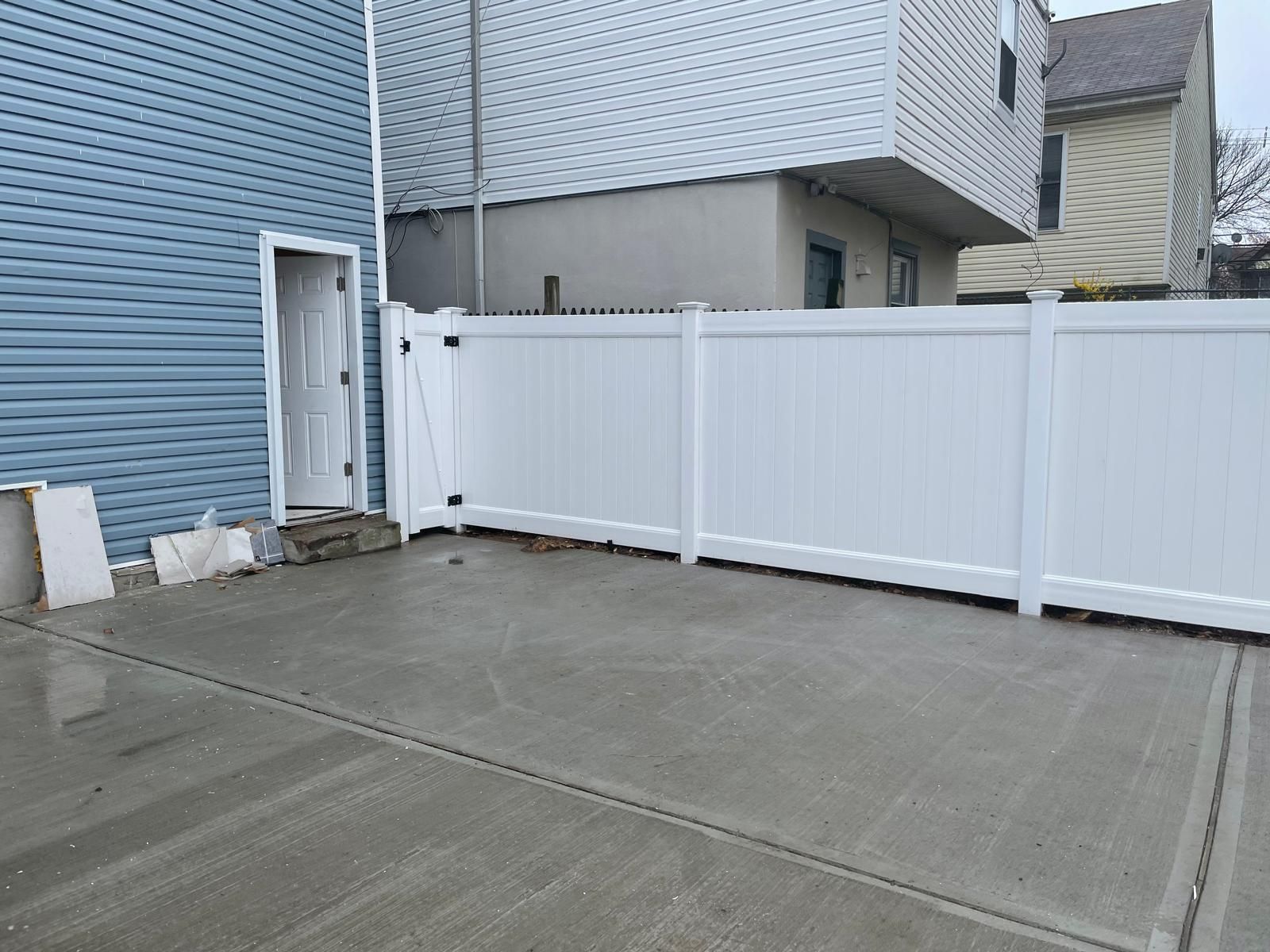 A white fence surrounds a concrete driveway in front of a house.