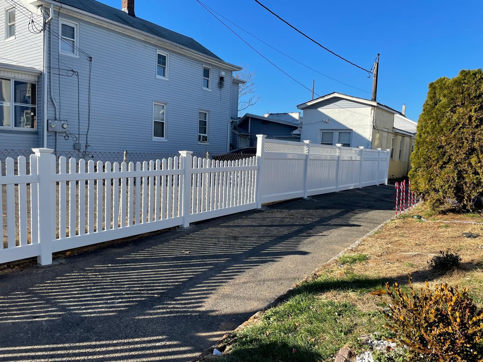 A white picket fence surrounds a driveway in front of a house.