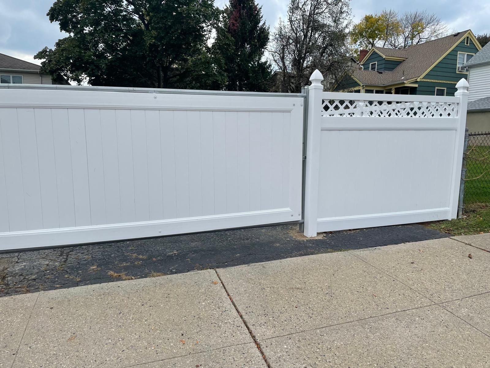 A white fence is sitting on a sidewalk next to a house.