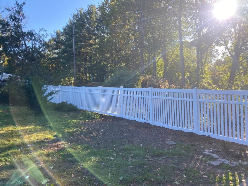 A white picket fence surrounds a yard with trees in the background.