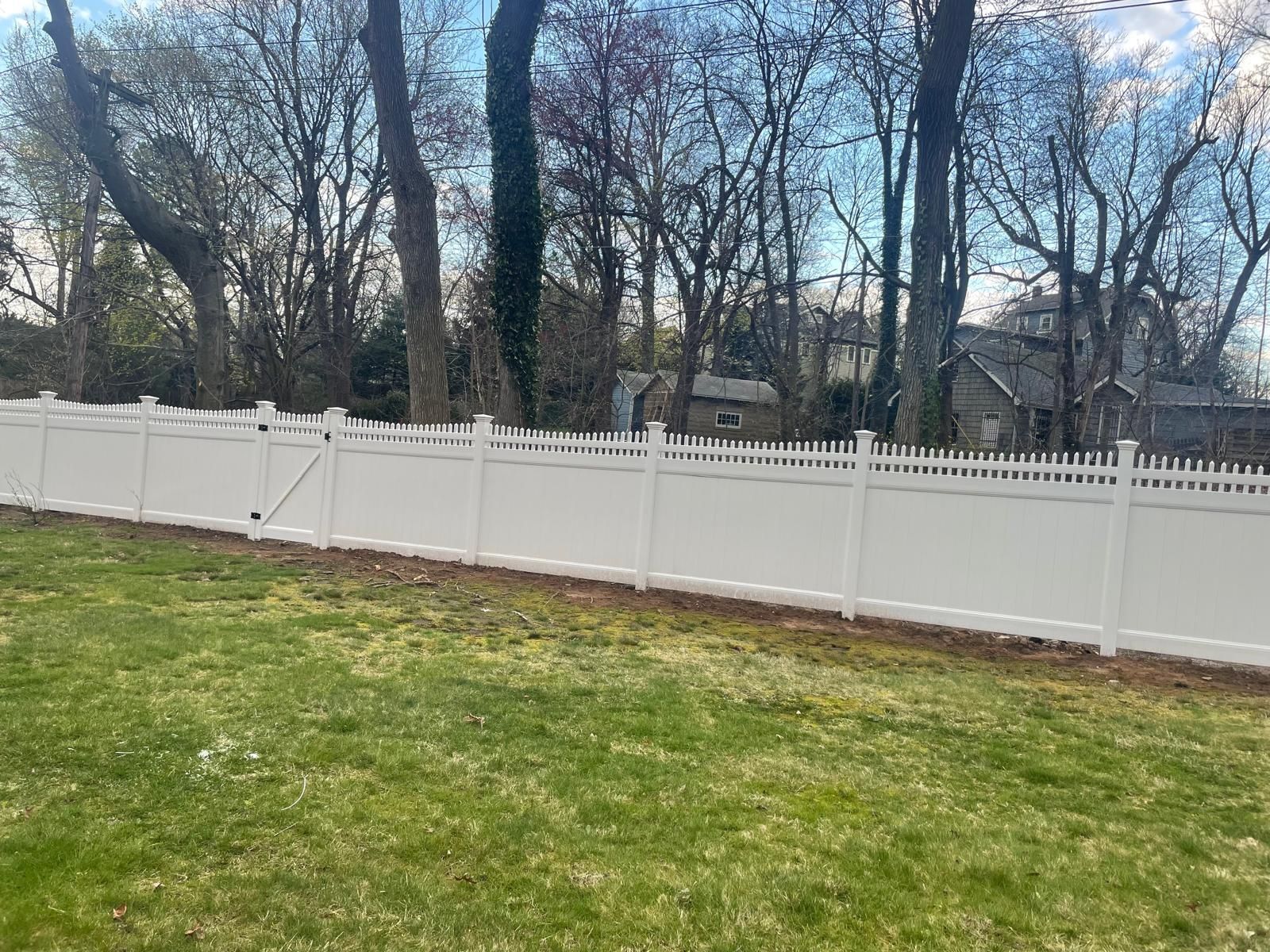 A white fence surrounds a lush green yard with trees in the background.