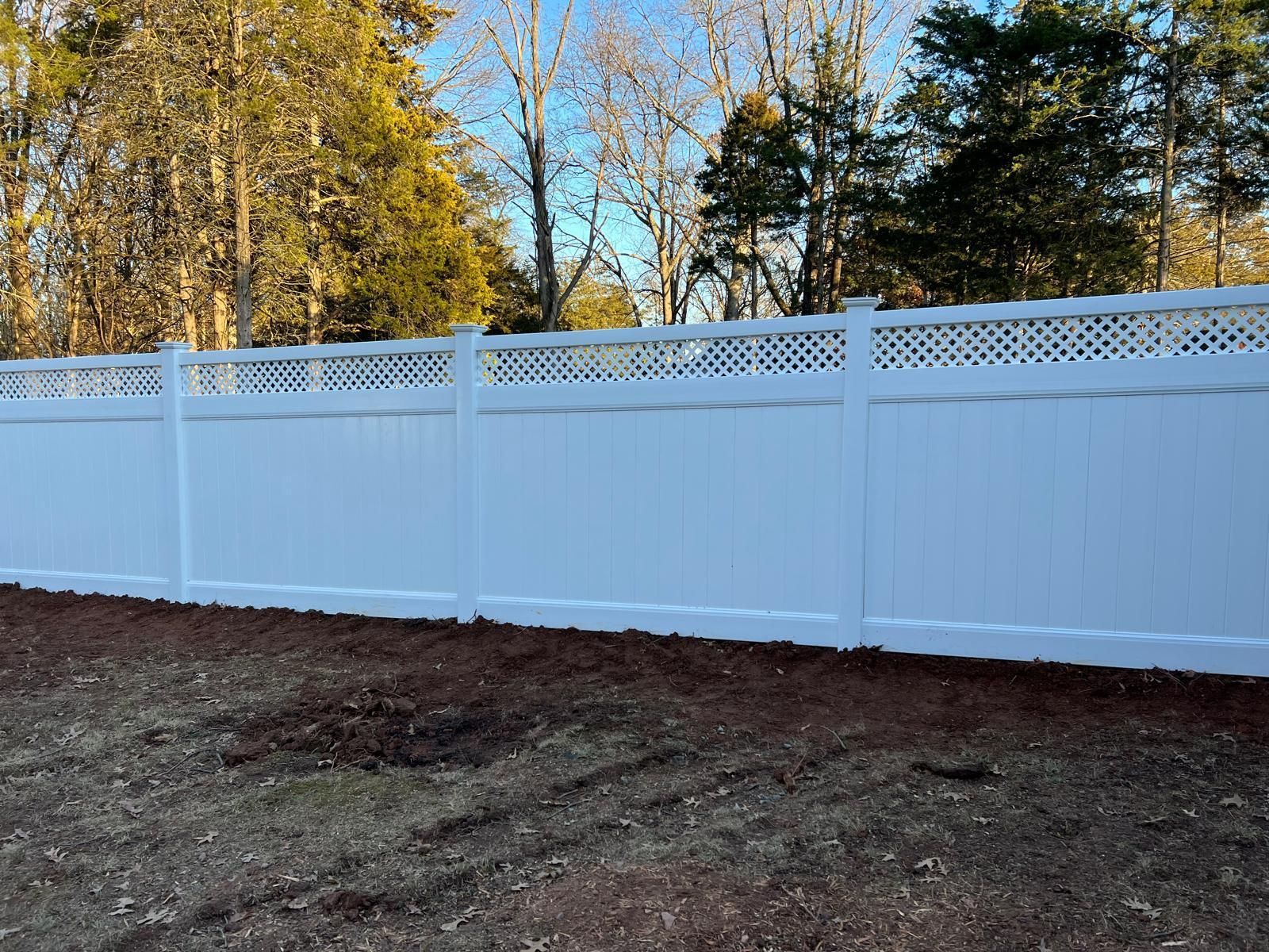 A white fence surrounds a yard with trees in the background.