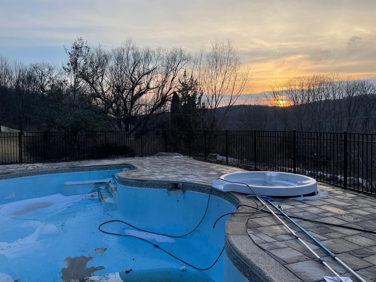 An empty swimming pool with a hot tub in the background and a sunset in the background.