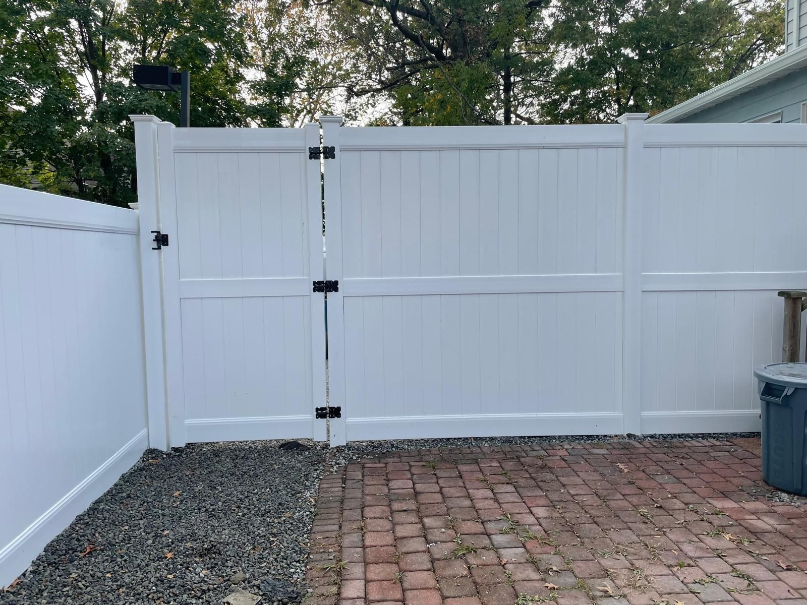 A white fence with a gate is sitting on top of a brick driveway.