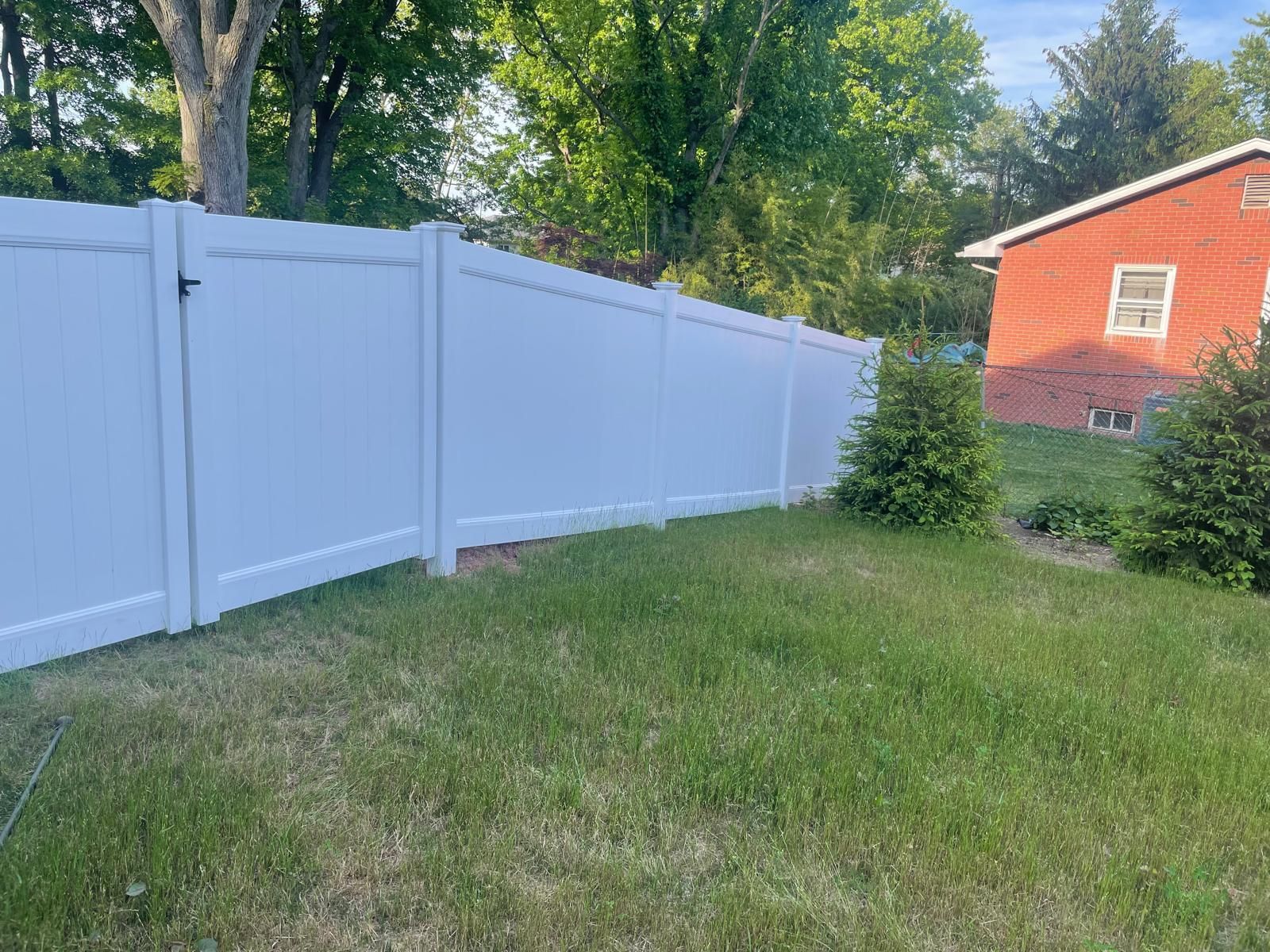 A white vinyl fence surrounds a lush green yard in front of a red house.