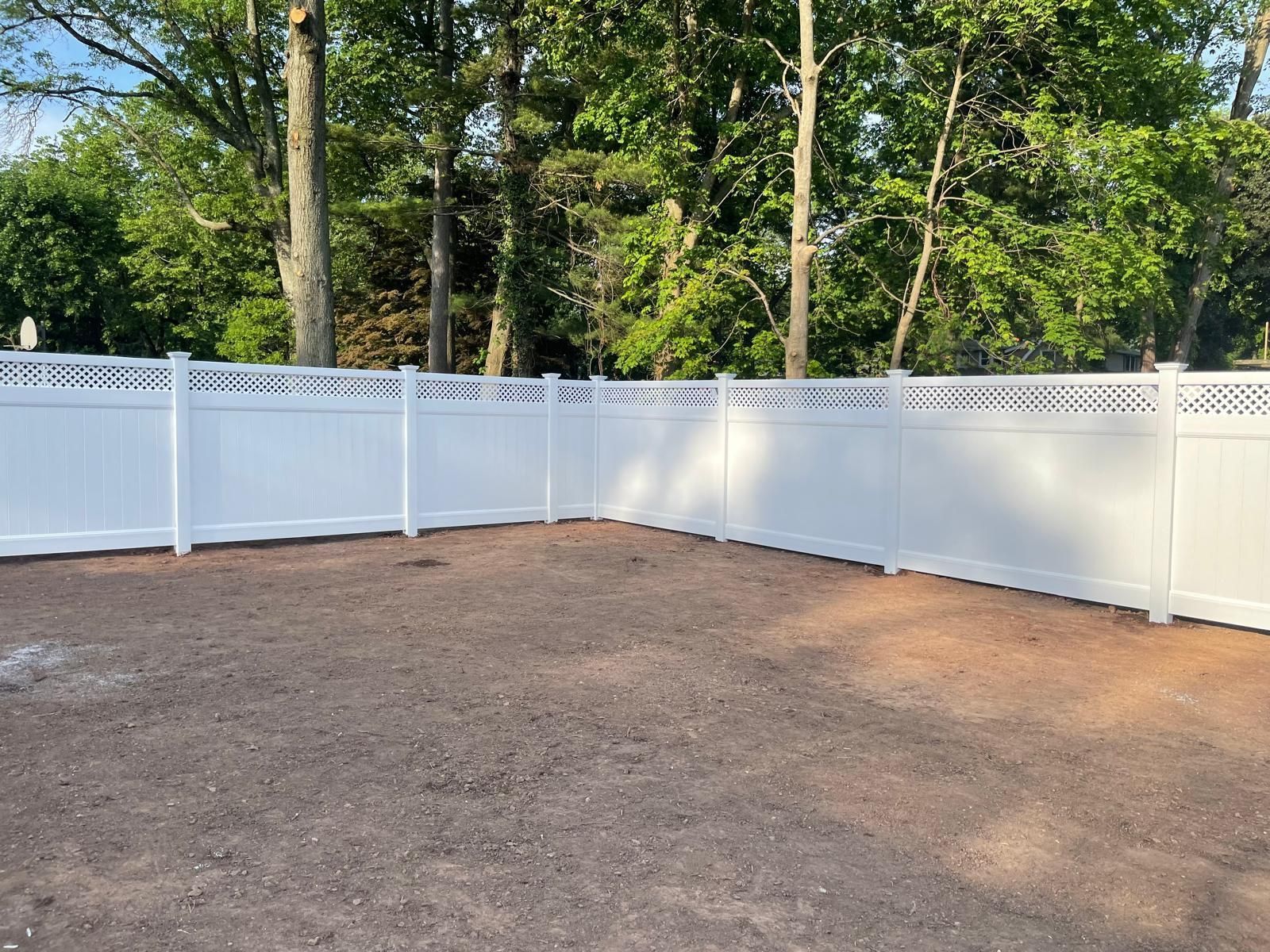 A white fence surrounds a dirt area with trees in the background.