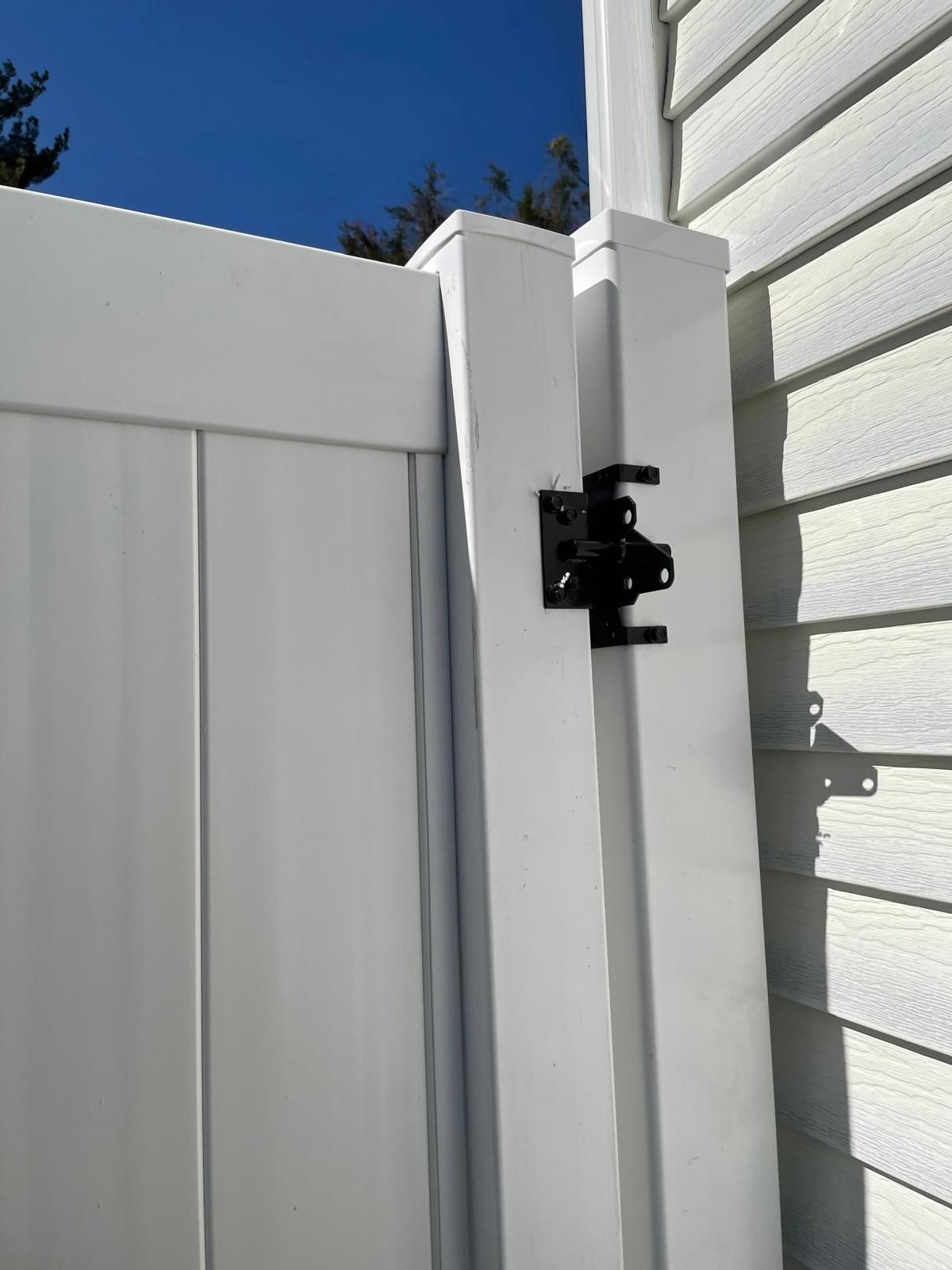 A white fence with a black latch is sitting next to a white house.
