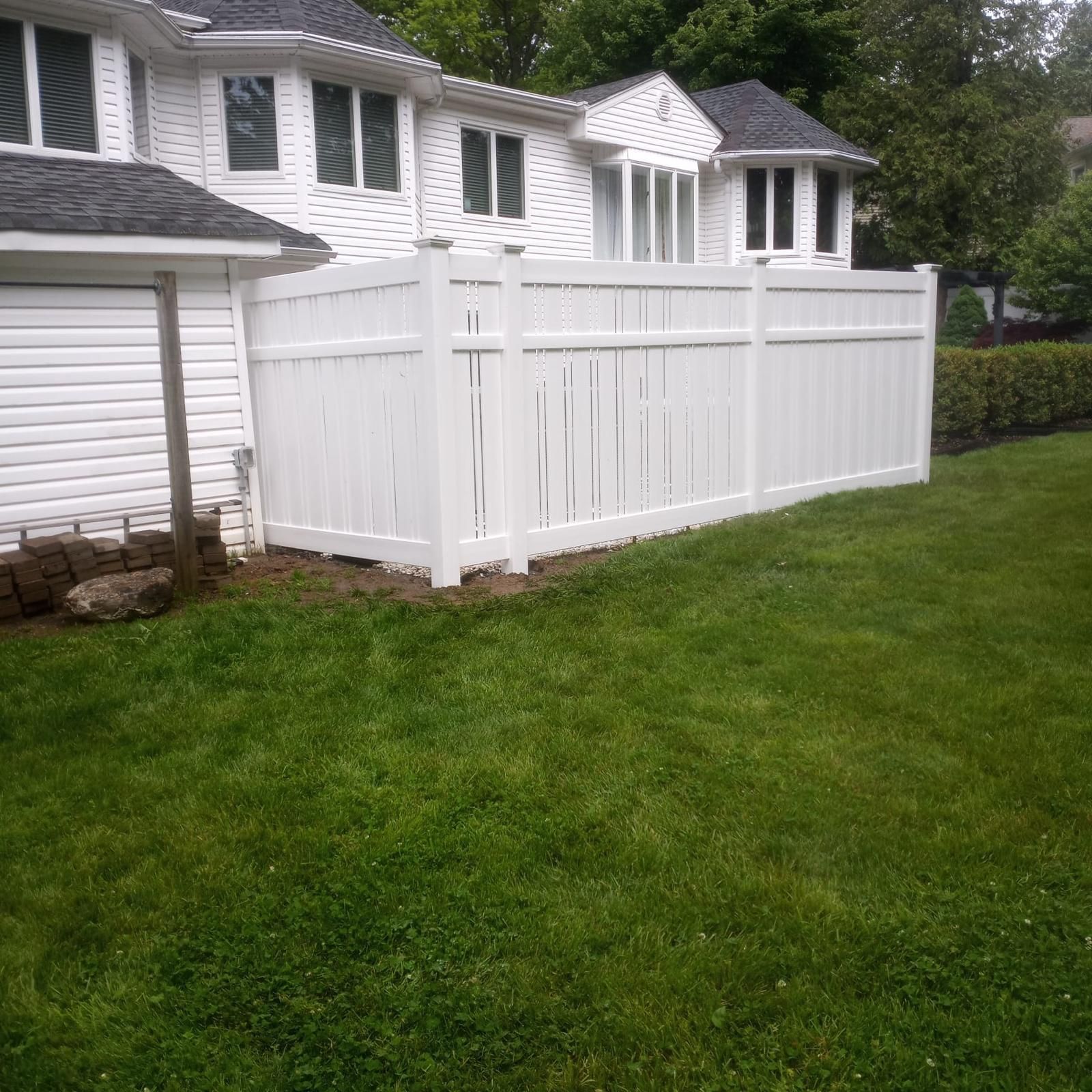 A white fence surrounds a lush green yard in front of a white house.