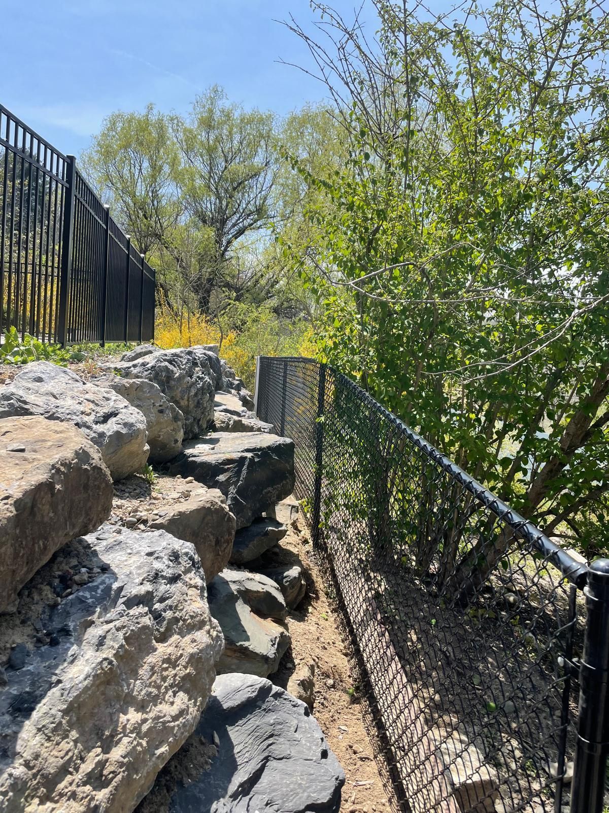 A chain link fence is surrounded by rocks and trees.