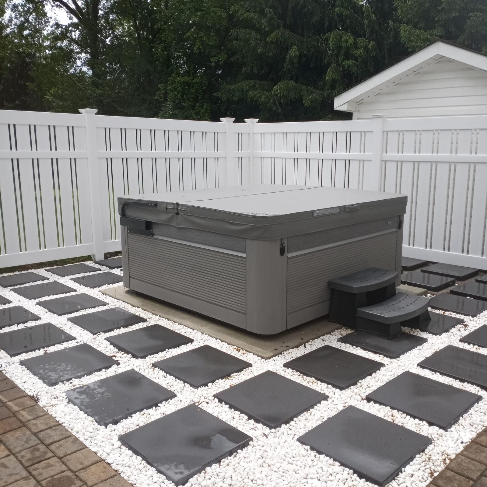 A hot tub is sitting on a patio next to a white fence