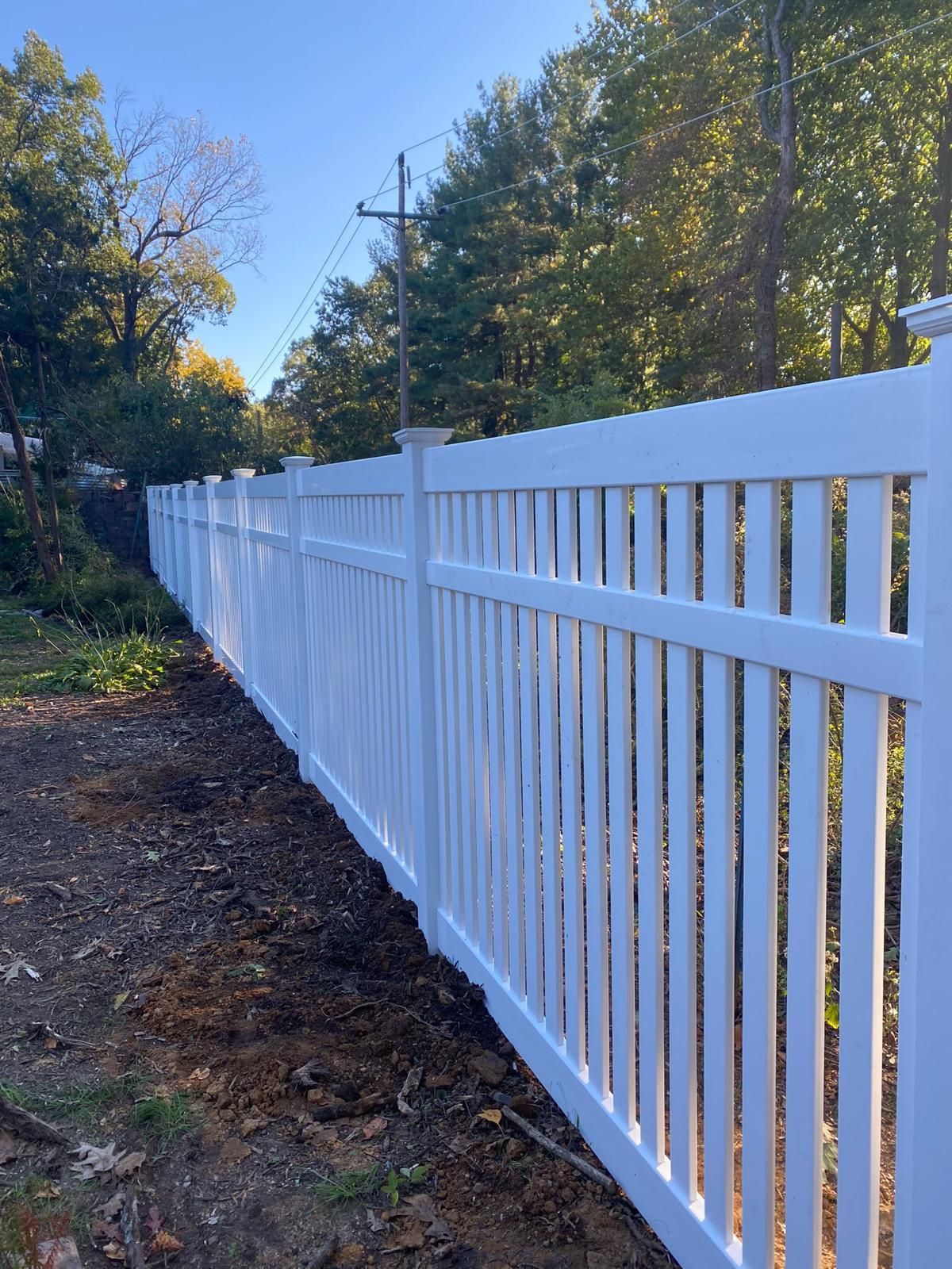 A white fence is surrounded by trees and dirt in a yard.