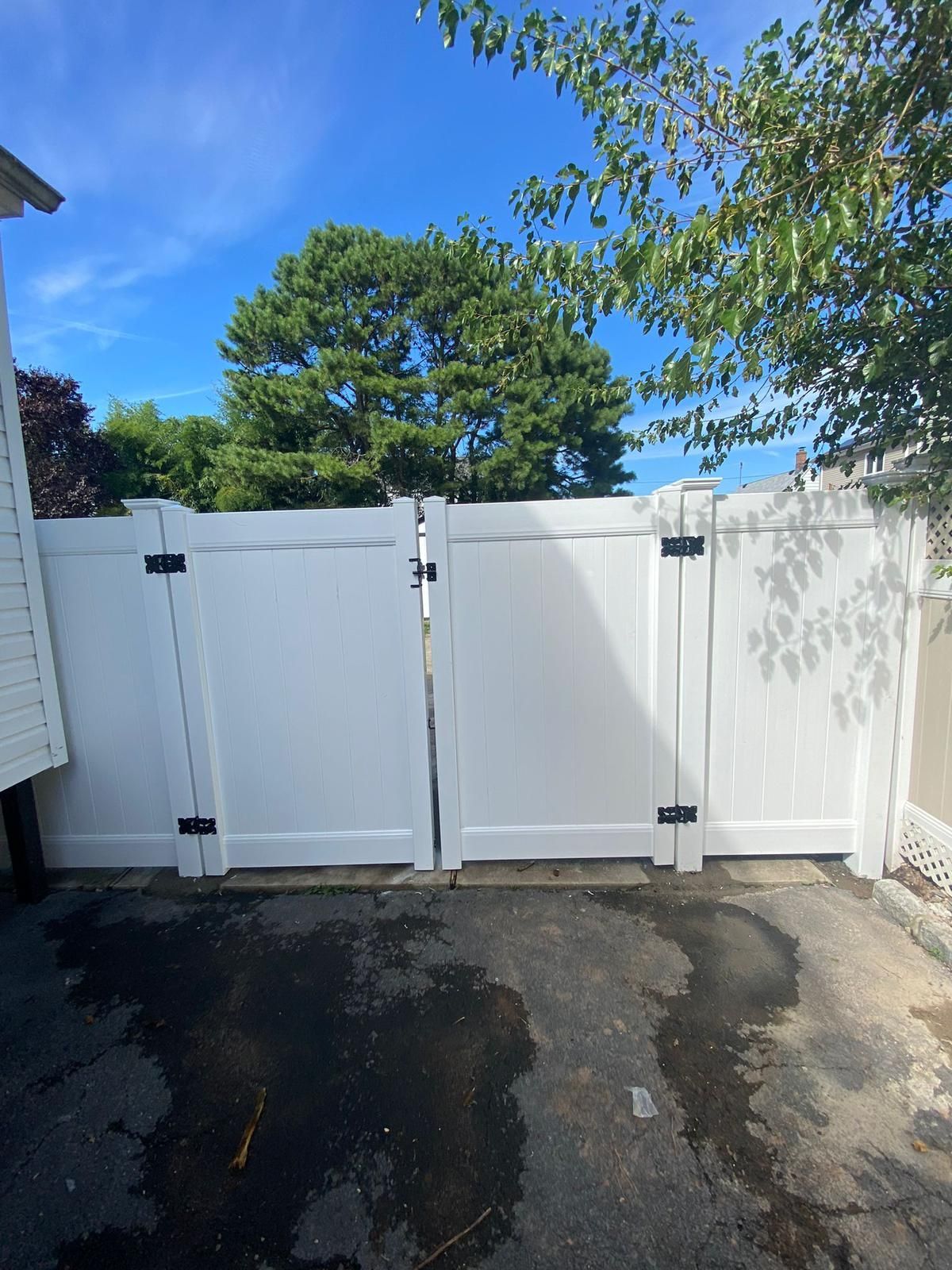 A white fence with two doors is sitting in a driveway.