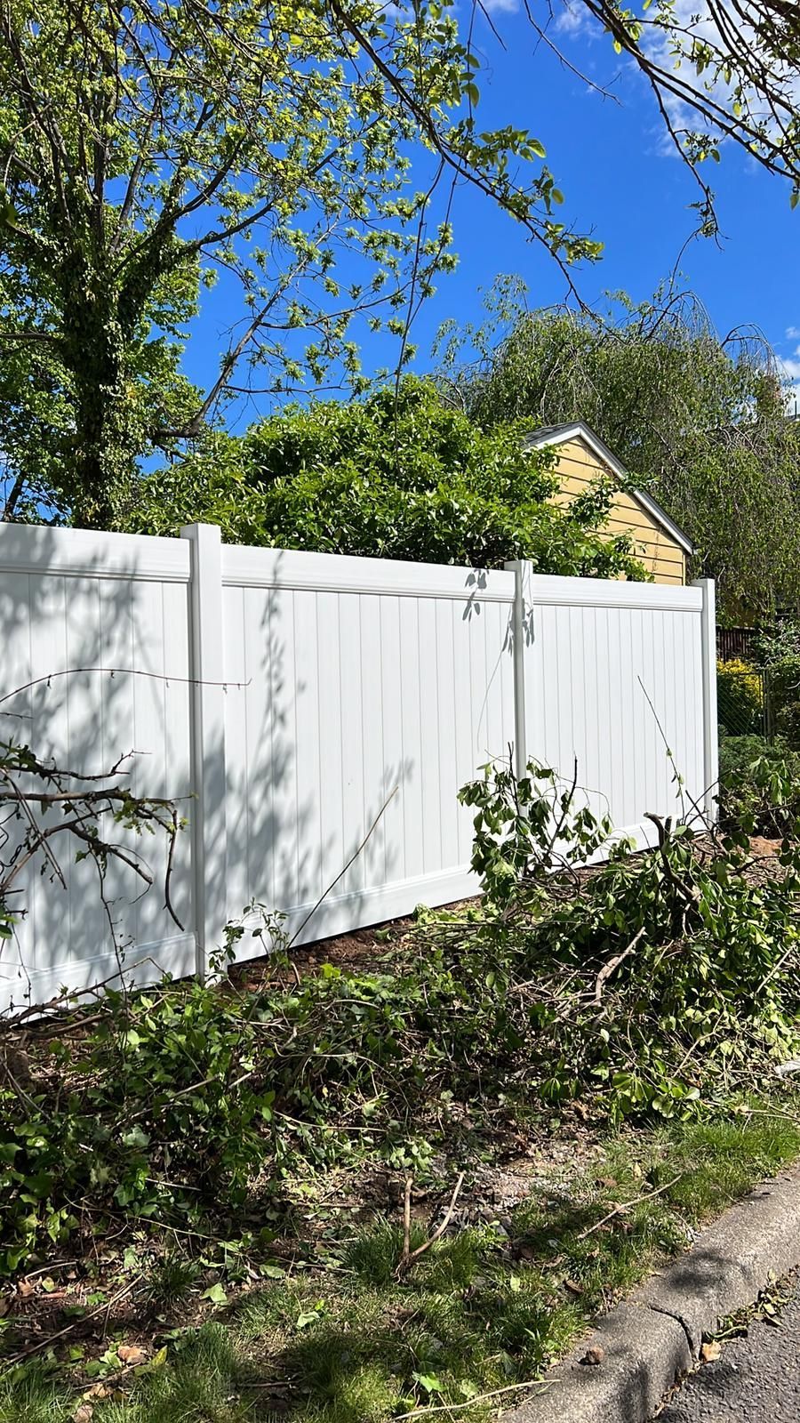 A white fence is surrounded by trees and bushes on a sunny day.