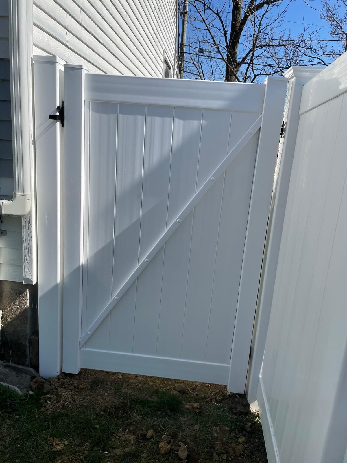 A white fence with a gate in the backyard of a house.