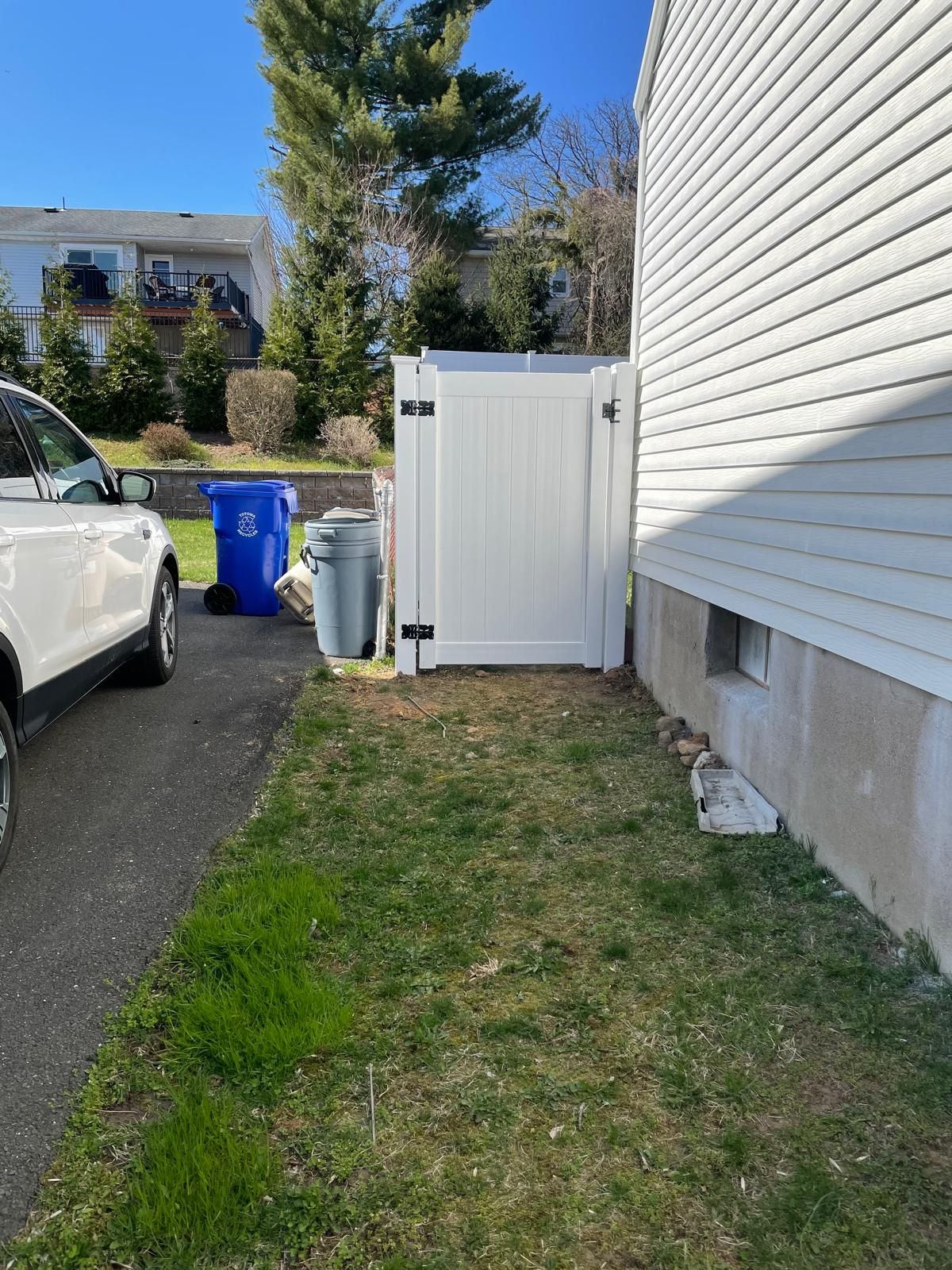 A white car is parked in a driveway next to a white house.
